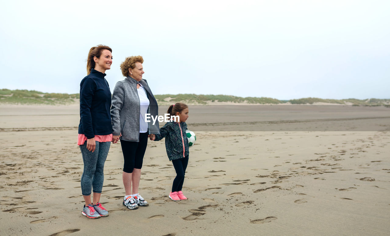 Woman standing with mother and daughter at beach against sky