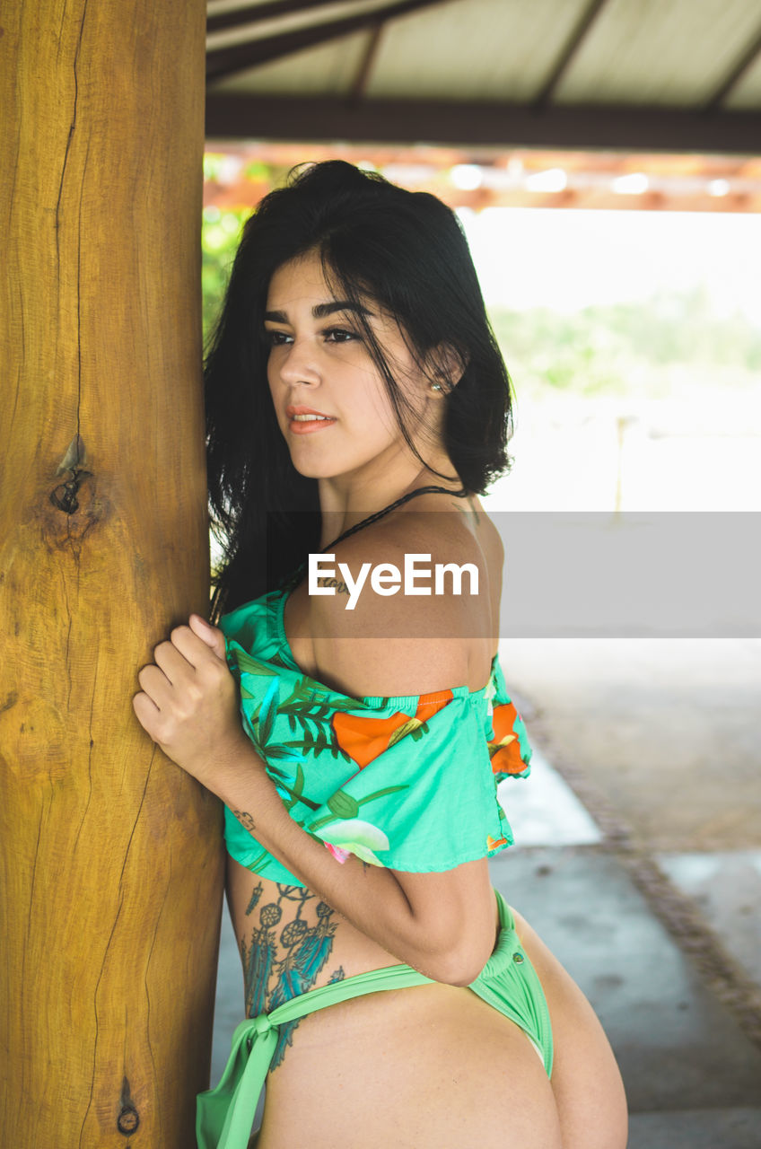 Seductive woman looking away while standing by pole