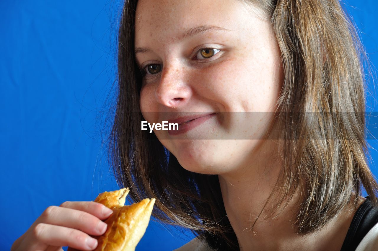 Close-up smiling woman eating food against blue background