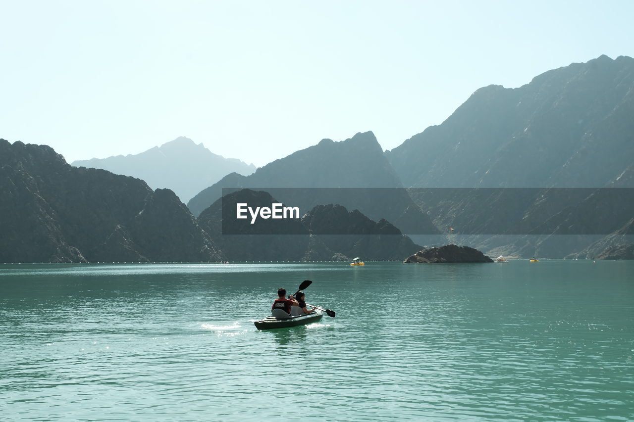 PEOPLE ON BOAT IN LAKE AGAINST MOUNTAIN