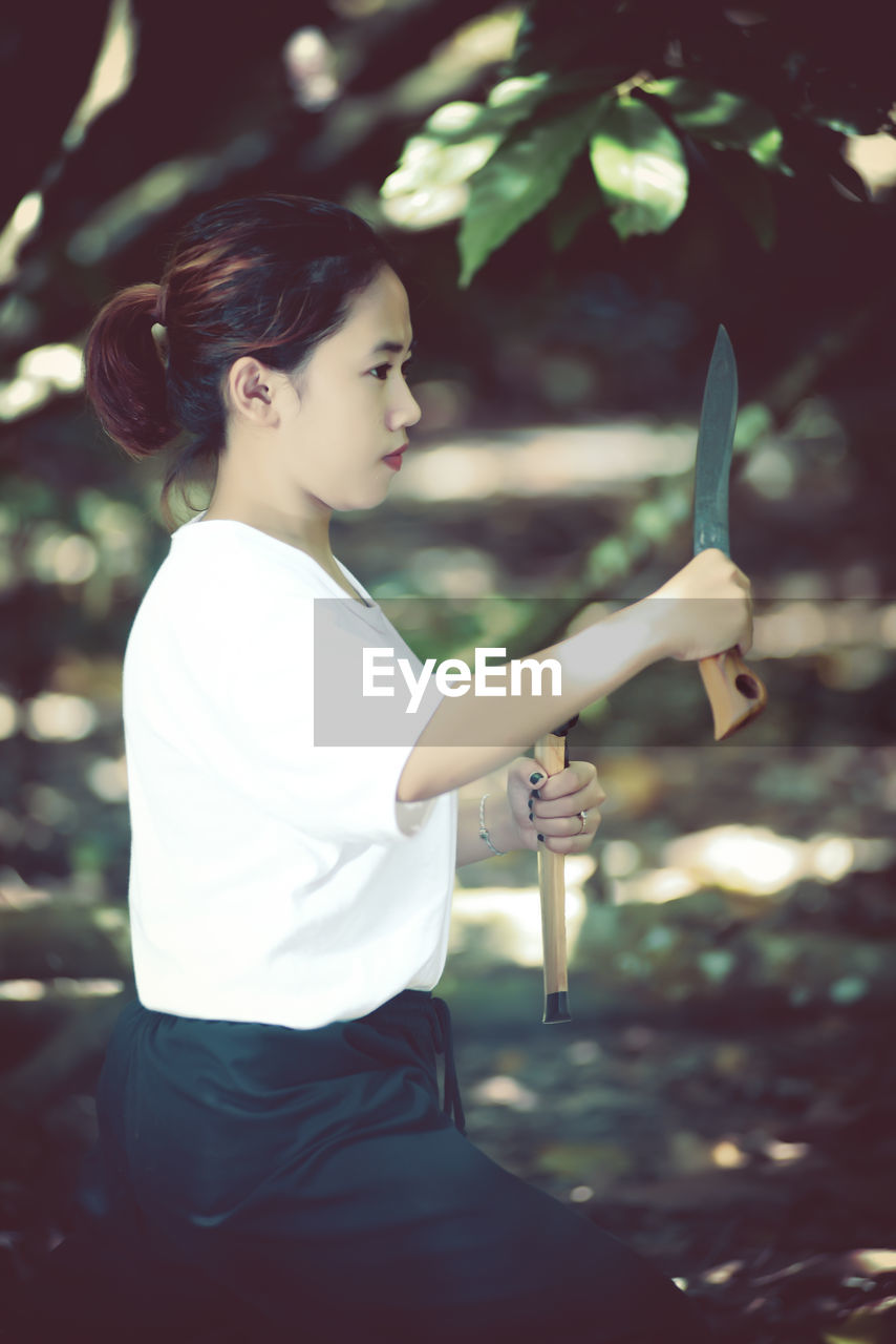 Side view of woman holding knife practicing martial arts outdoors