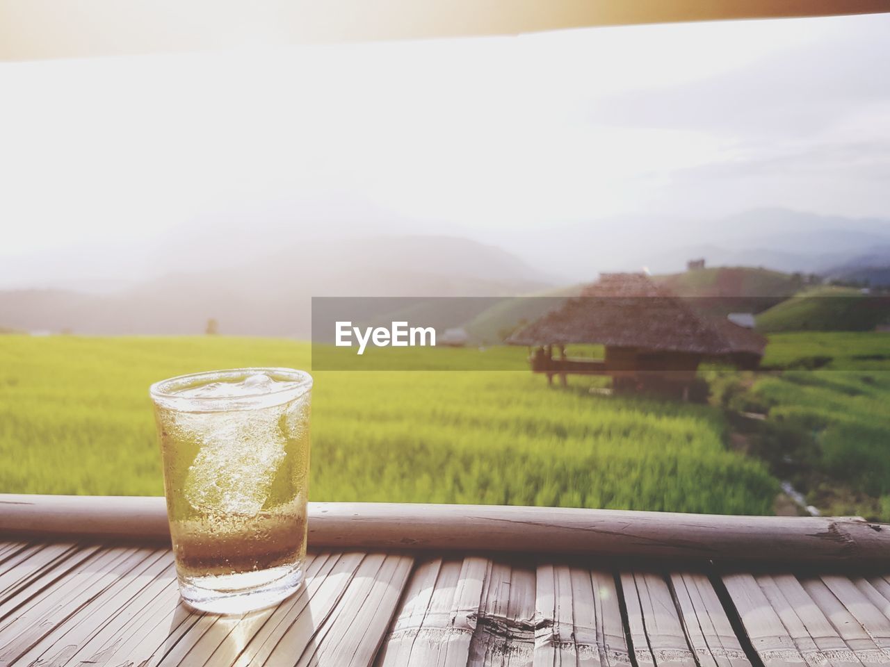 Drink in glass on wooden table against agricultural field