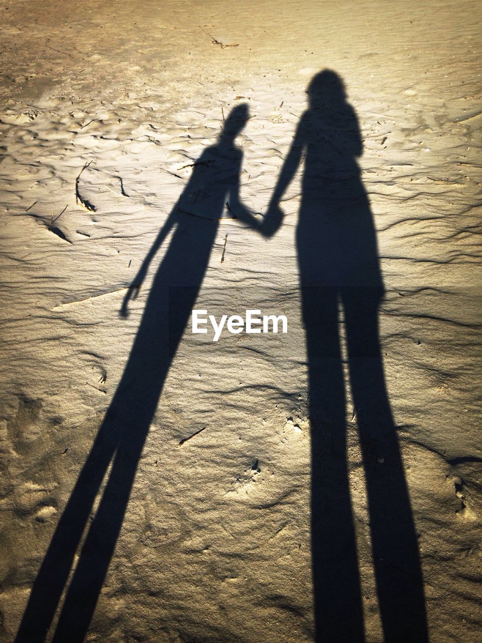 Shadow of mother and daughter holding hands at beach
