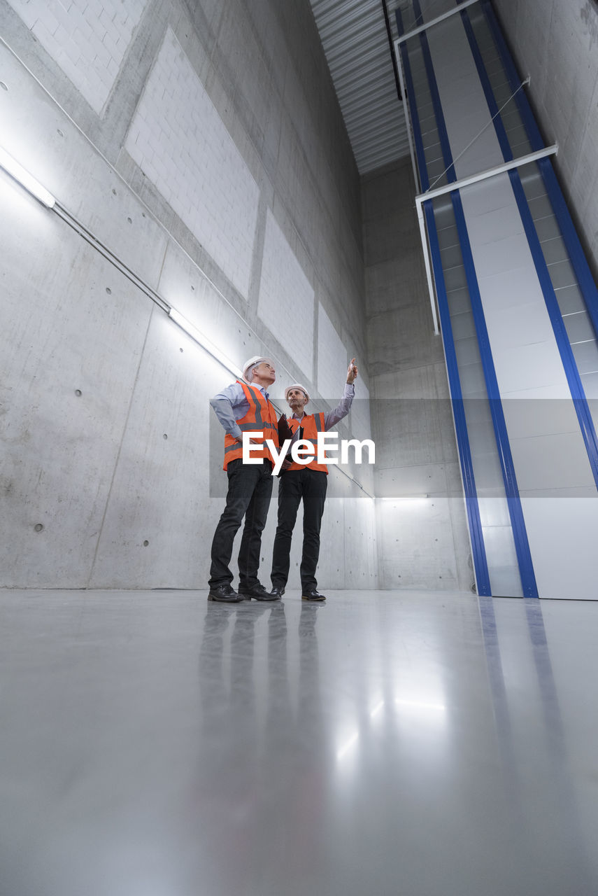 Two colleagues wearing safety vests and hard hats talking in a building