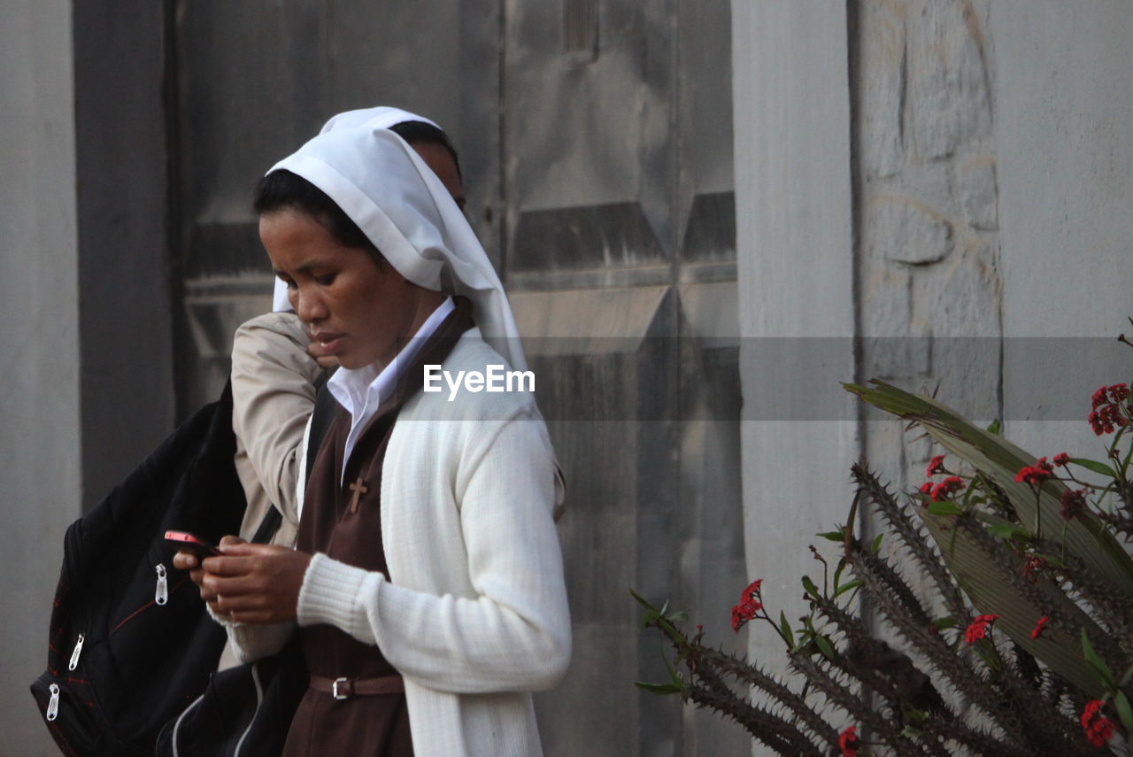 YOUNG WOMAN USING MOBILE PHONE WHILE STANDING ON CAMERA