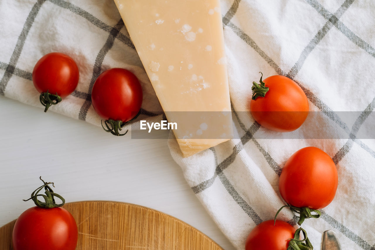 Cherry tomatoes and a piece of parmesan cheese on the table with a kitchen towel and a cutting board