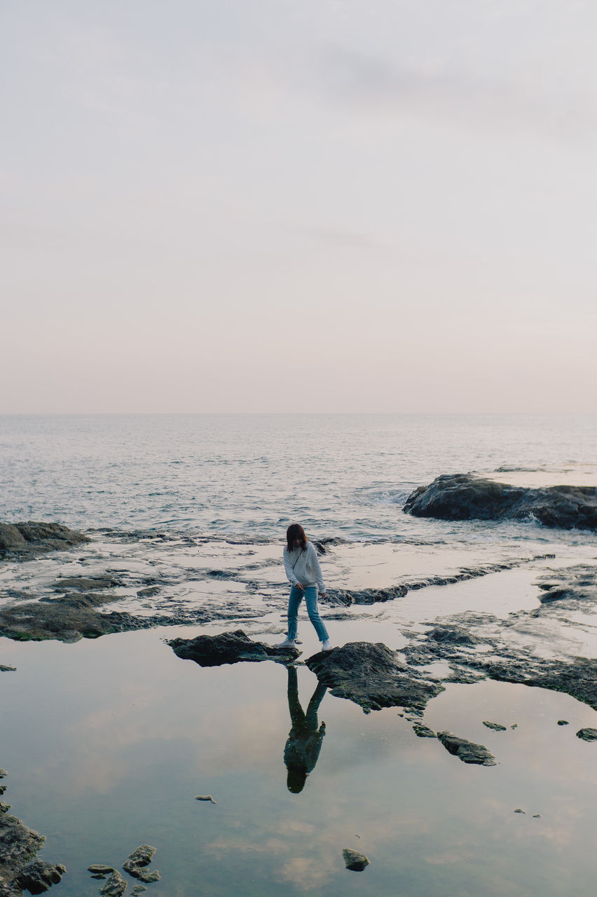 Rear view of woman standing at beach against sky