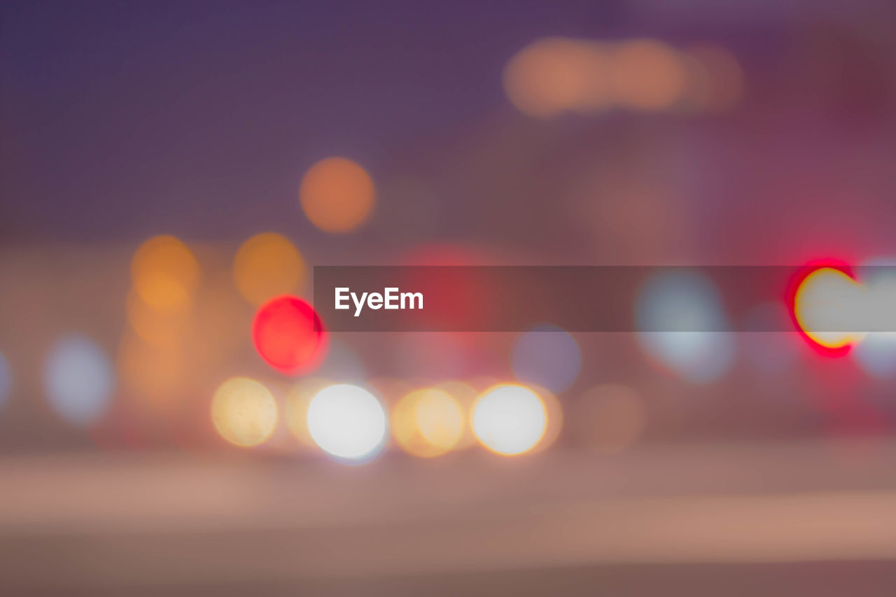DEFOCUSED IMAGE OF ILLUMINATED LIGHTS AGAINST SKY AT NIGHT