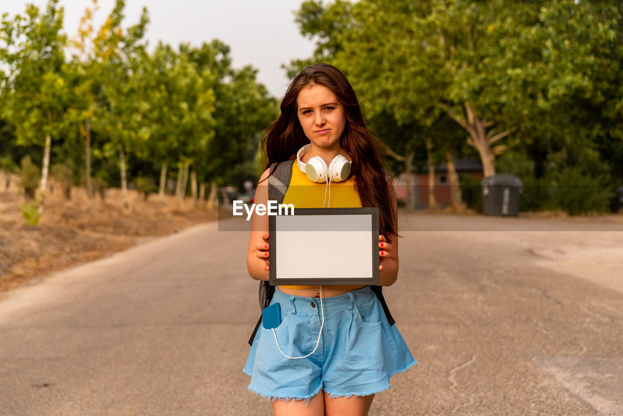 Young caucasian girl showing blank board in the park