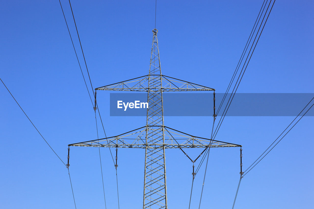 Low angle view of electricity pylon against clear blue sky