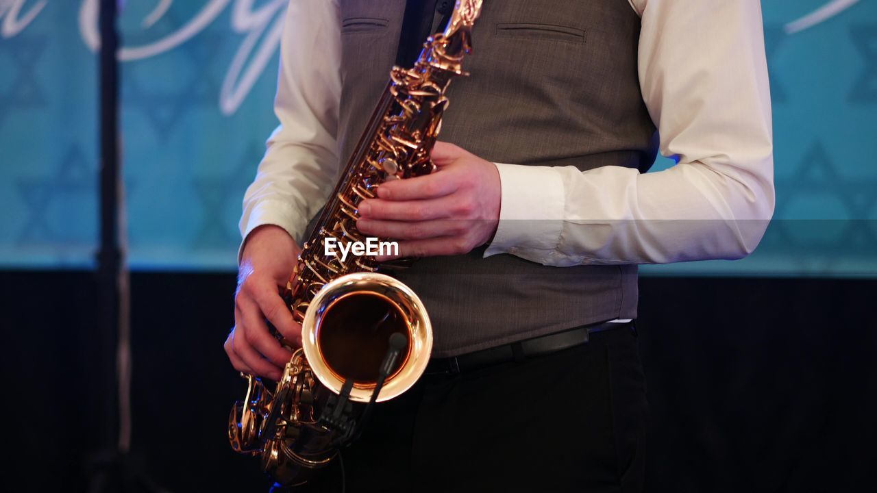 Midsection of man playing saxophone against wall