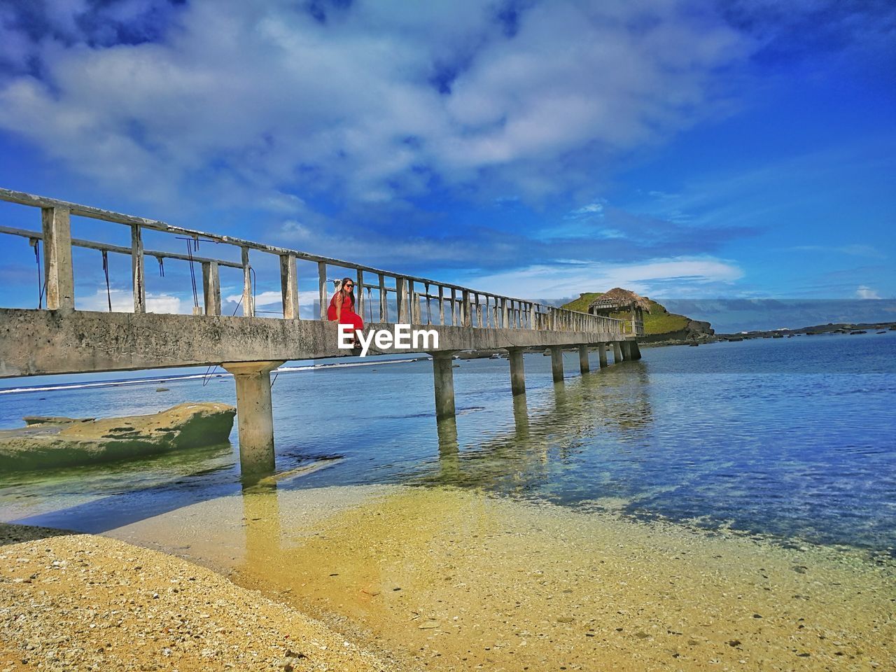 Woman sitting on bridge over sea against sky