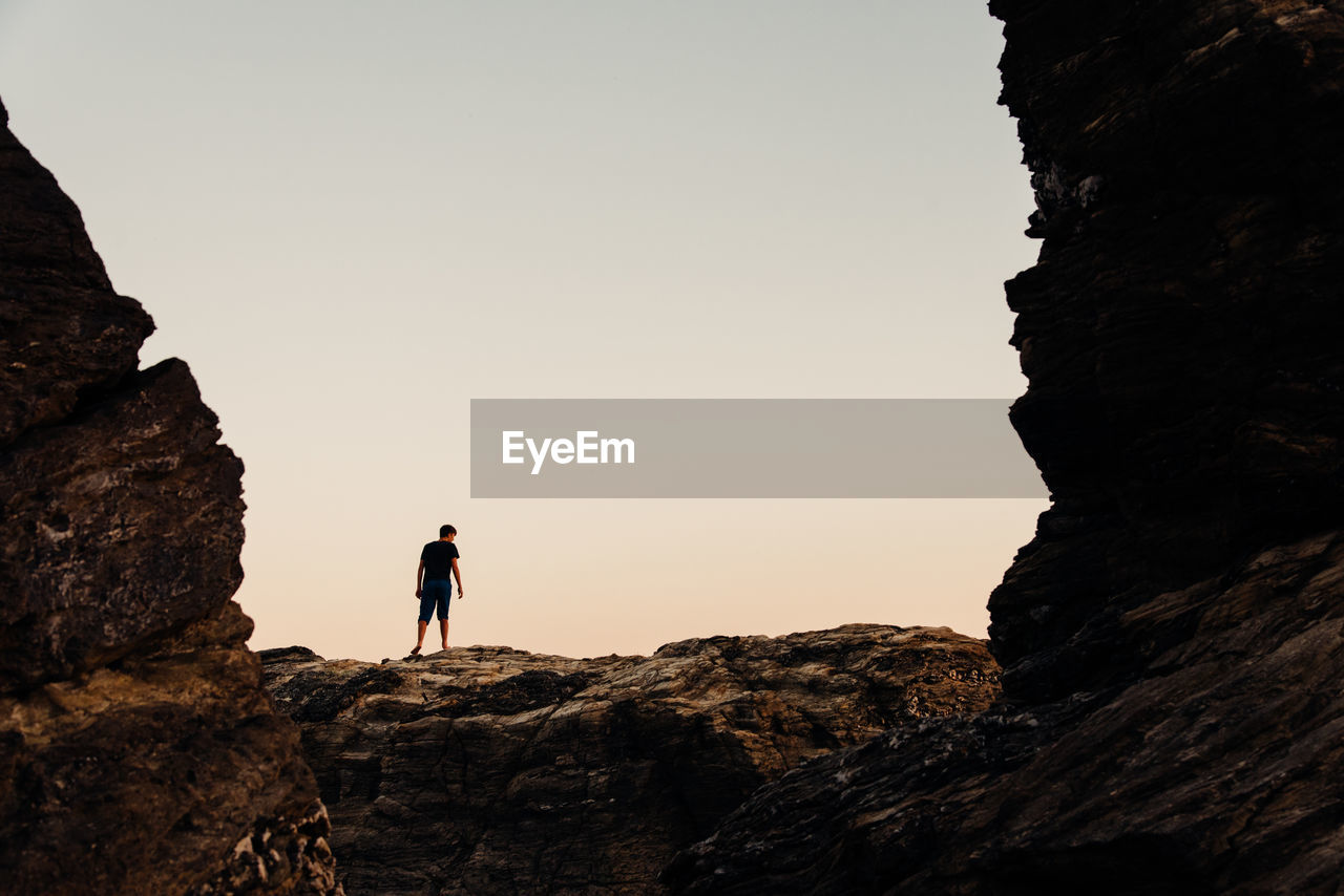 Low angle view of man standing on rock against sky