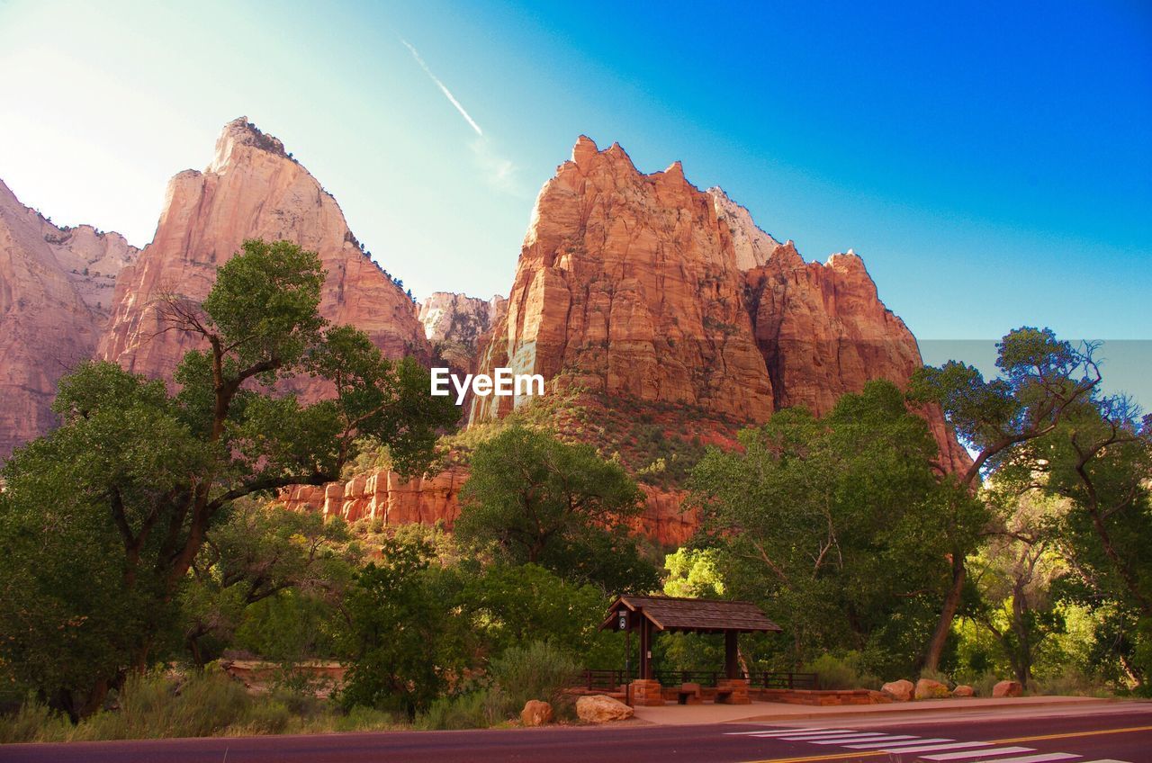 Low angle view of trees and rocky mountains against blue sky