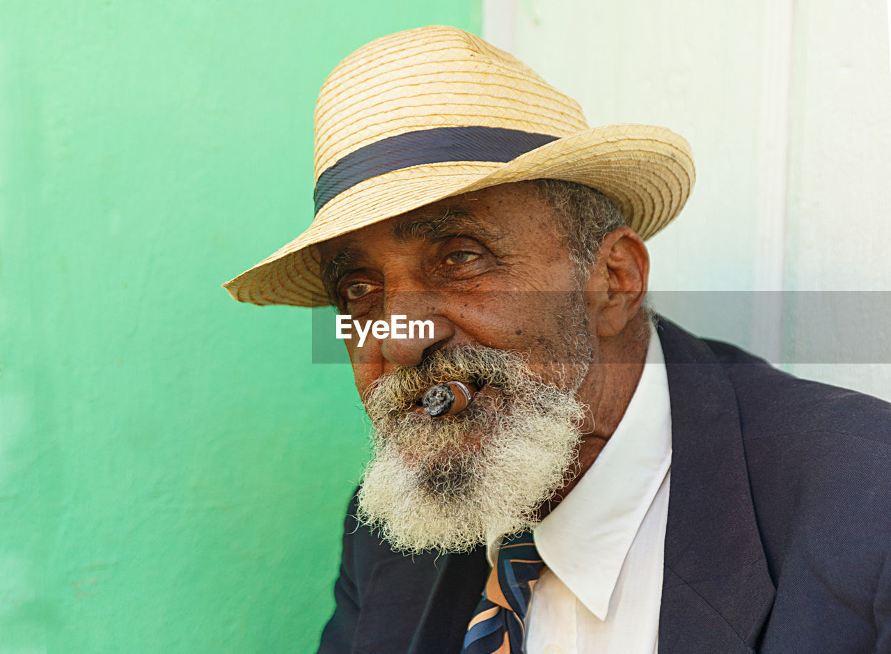 Portrait of man smoking cigar while sitting against wall
