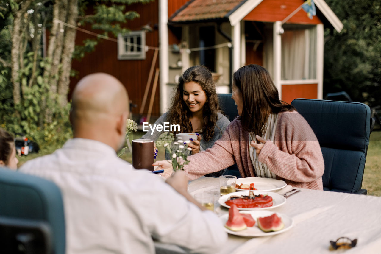 Smiling woman talking to daughter while sitting by dining table in yard