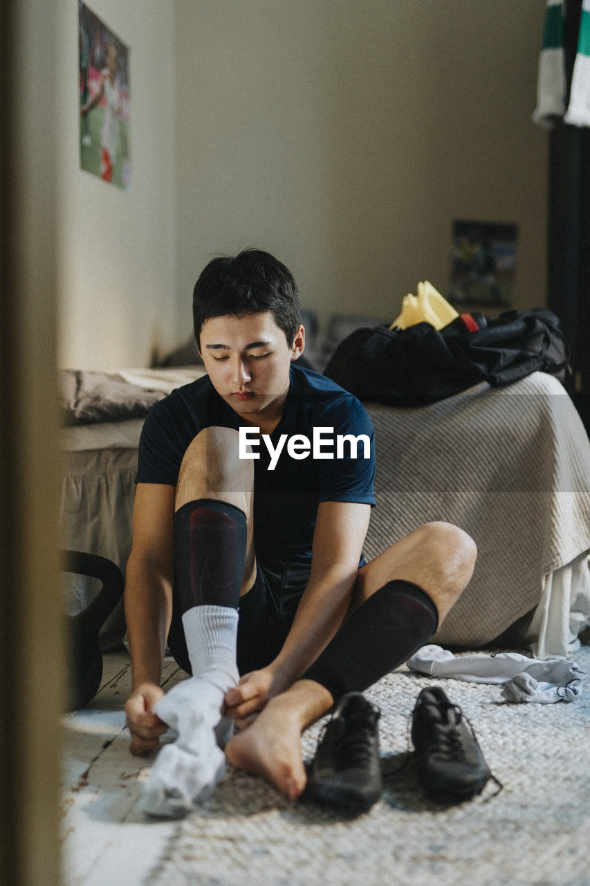 Teenage boy wearing sock while sitting on carpet at home