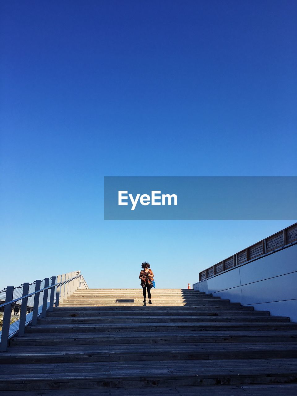 Low angle view of woman walking on steps against clear sky