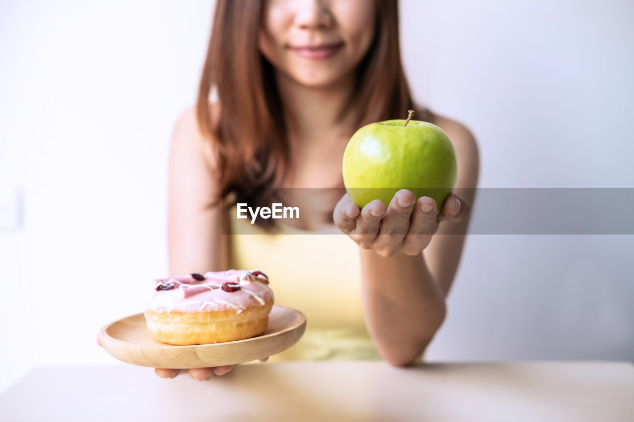Midsection of woman holding apple and donut while sitting at table