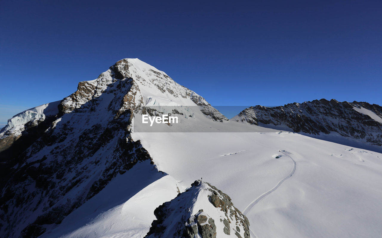Low angle view of snow covered mountains against blue sky