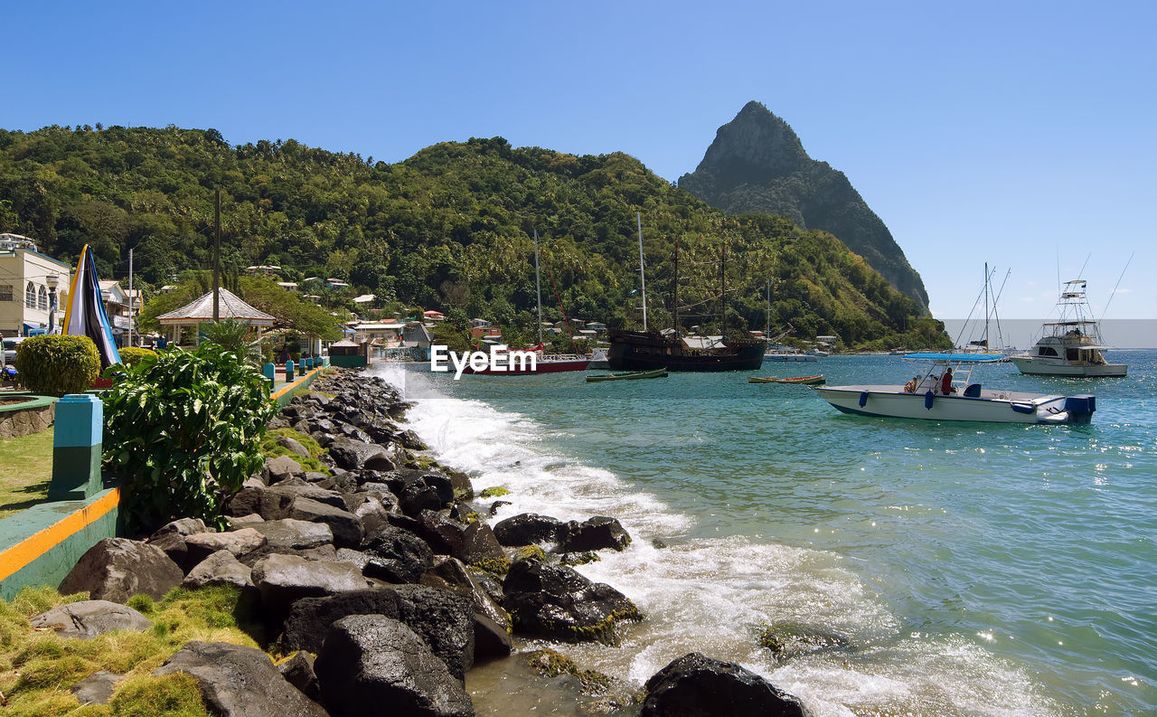 BOATS MOORED ON SEA BY MOUNTAIN AGAINST CLEAR SKY