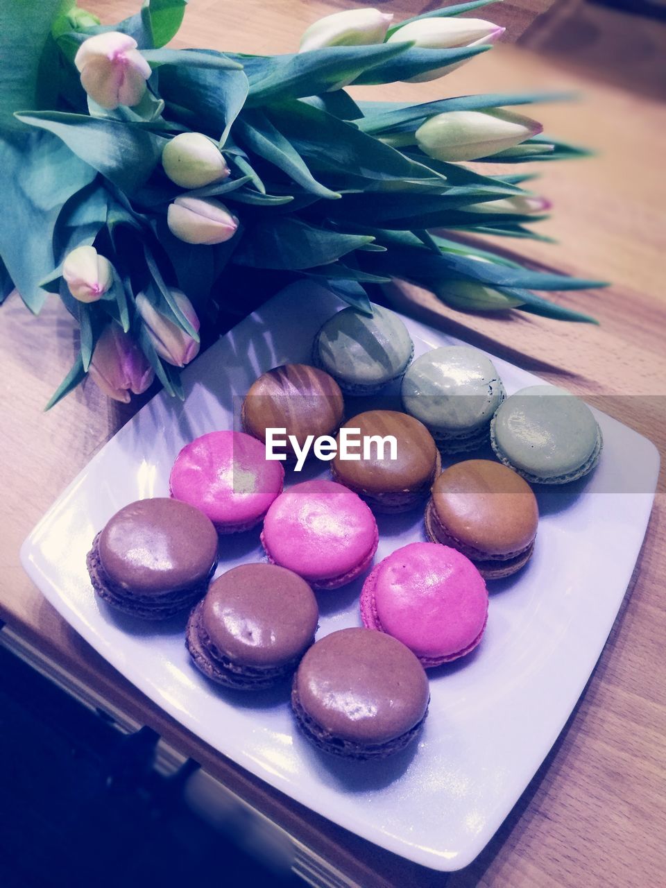 High angle view of colorful macaroons in plate by flowers on table