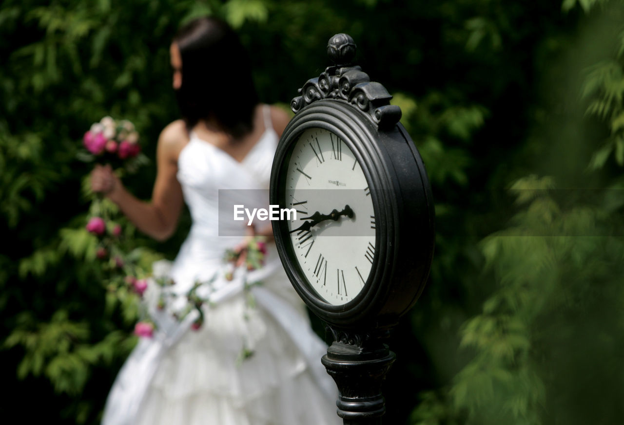 Close-up of clock with bride standing in background