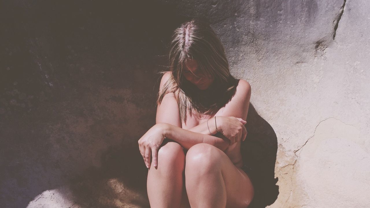 Sensuous topless woman sitting against wall