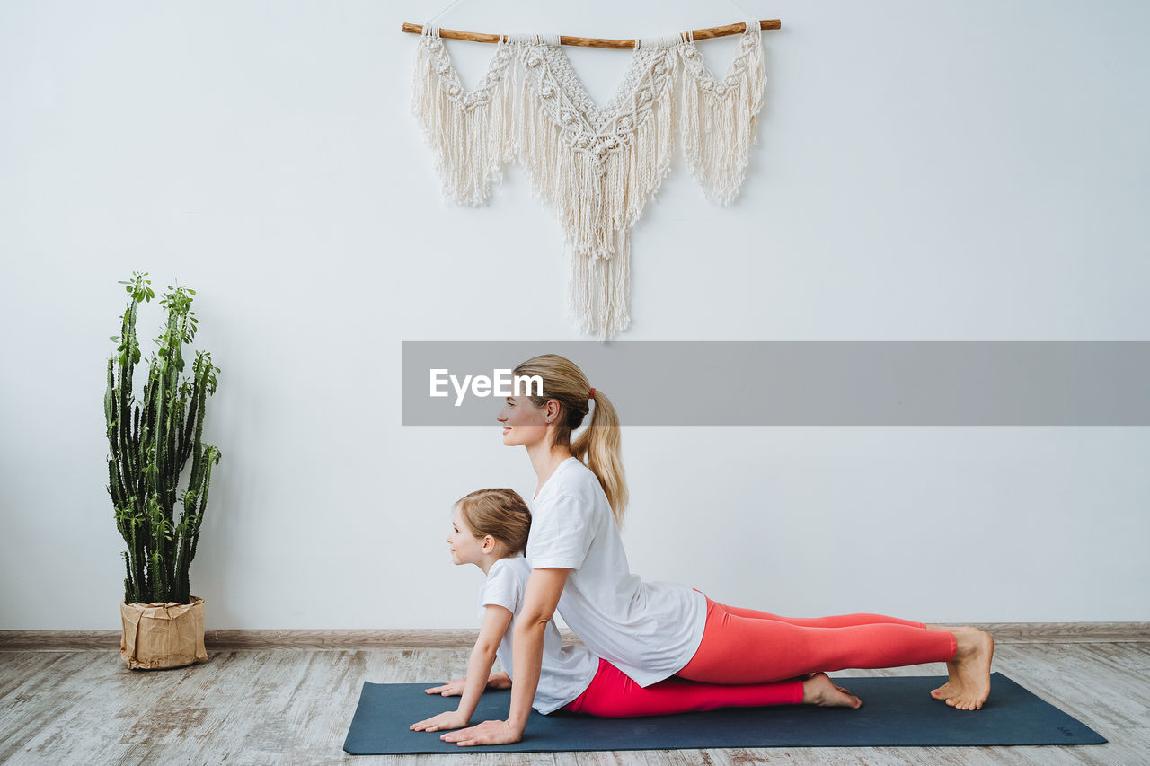 full length of young woman exercising on table against white background