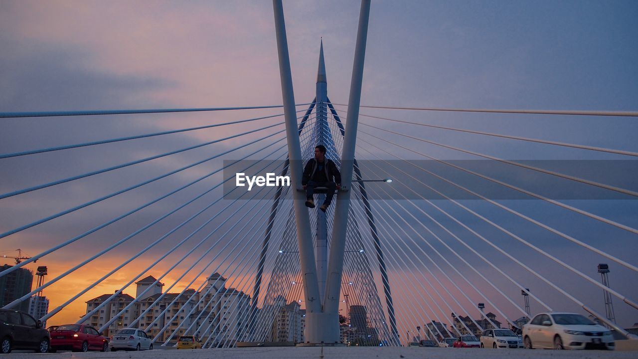 LOW ANGLE VIEW OF SUSPENSION BRIDGE CABLES AGAINST SKY DURING SUNSET