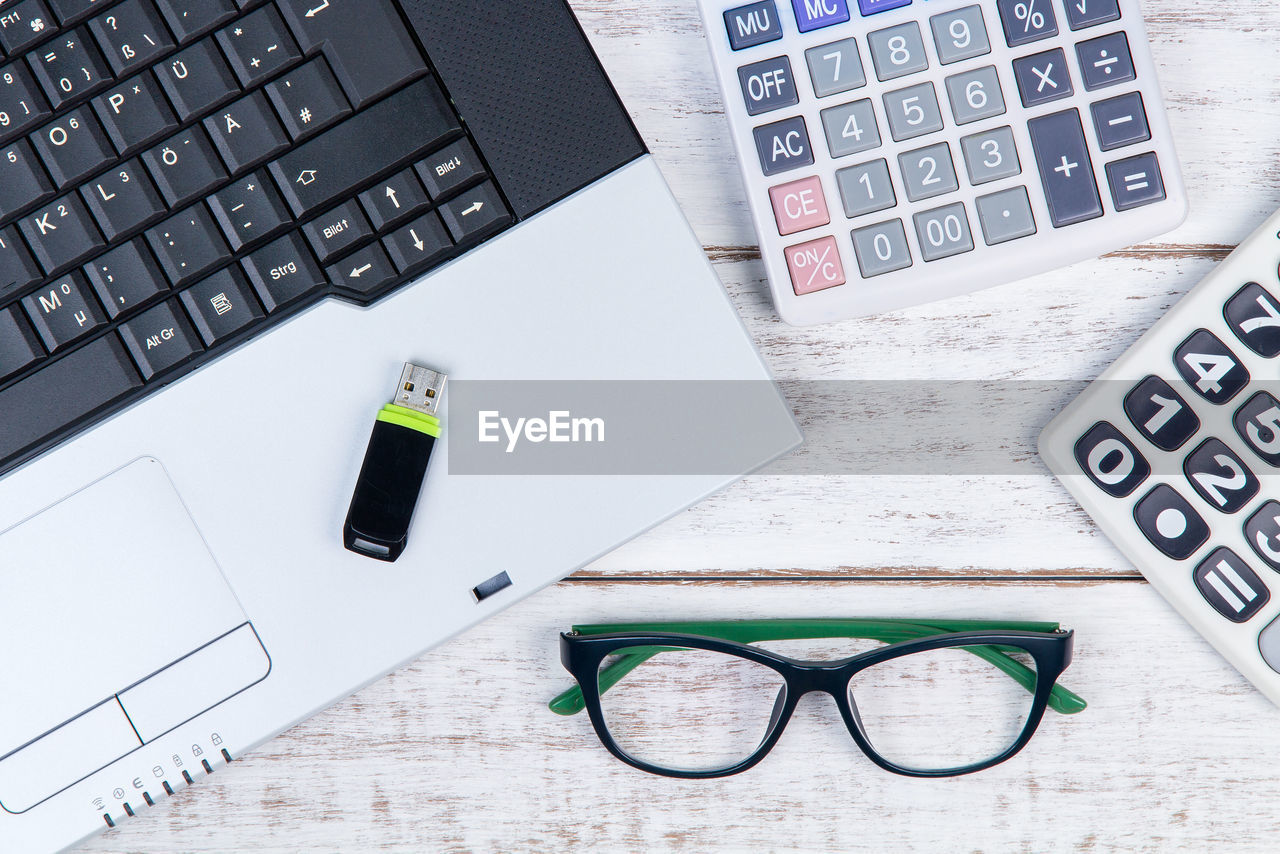 Directly above shot of laptop with eyeglasses and stationary on white table