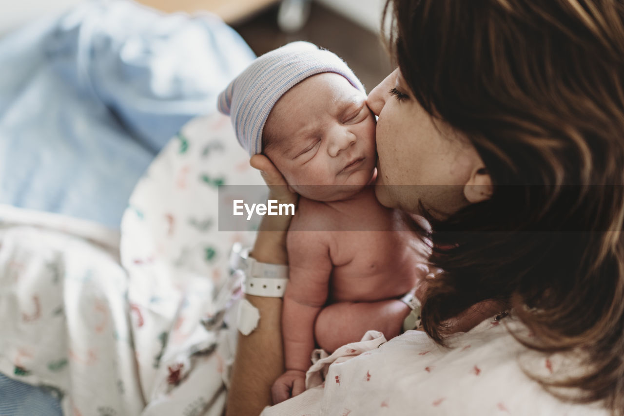 Close up detail of mother kissing newborn son's cheek in hospital negative space