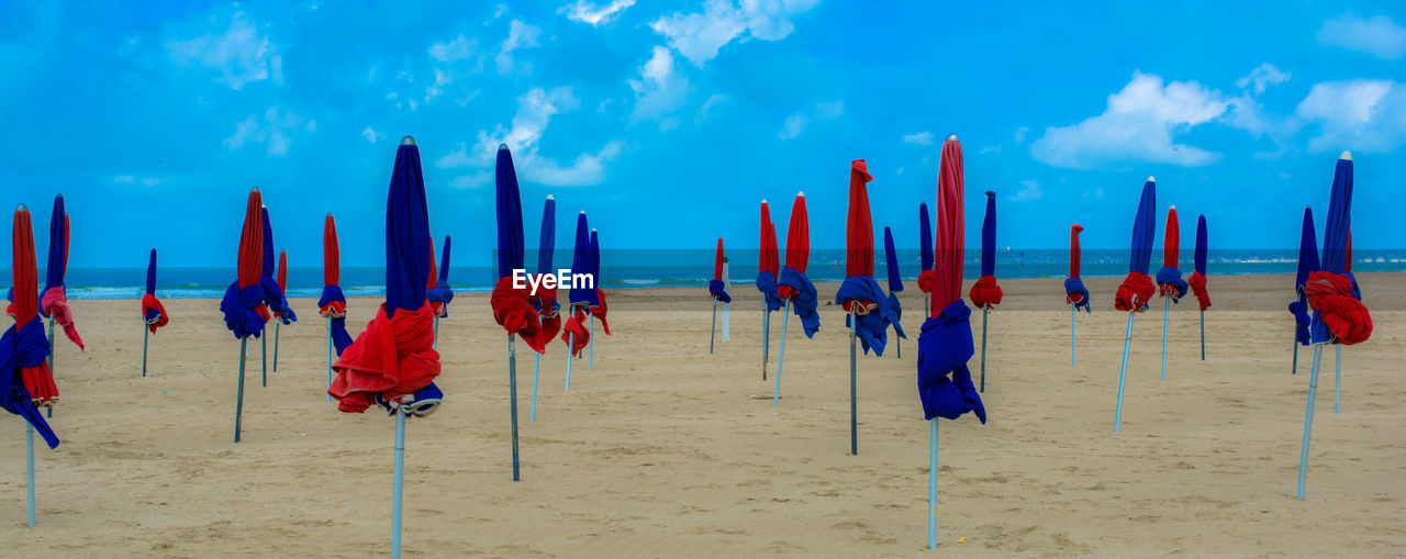 Panoramic view of closed parasols at beach against sky