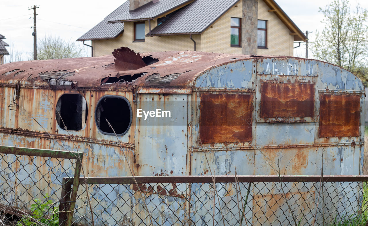architecture, abandoned, metal, damaged, built structure, building exterior, rusty, rundown, fence, old, no people, shack, transport, building, nature, tree, day, house, decline, deterioration, weathered, rust, vehicle, sky, outdoors, bad condition, broken