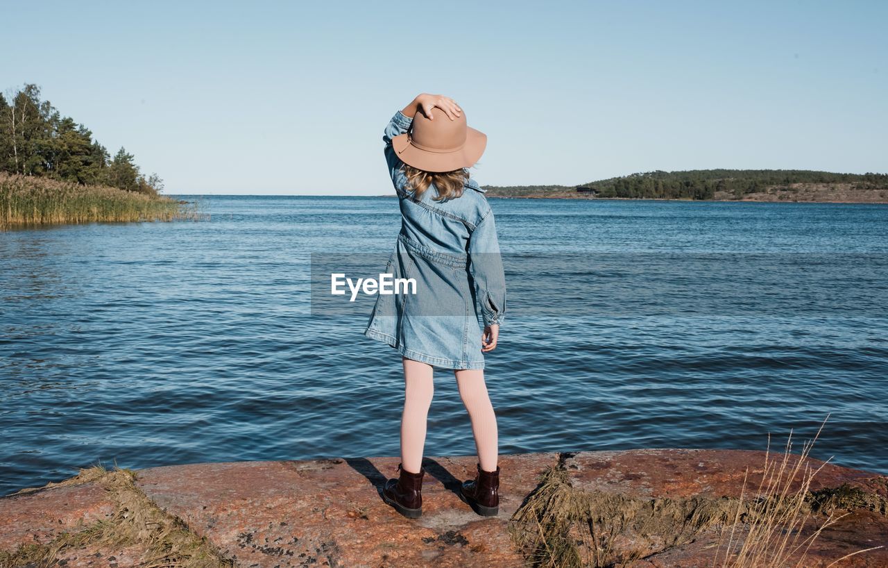 Young girl holding onto her hat whilst looking out at the finish sea