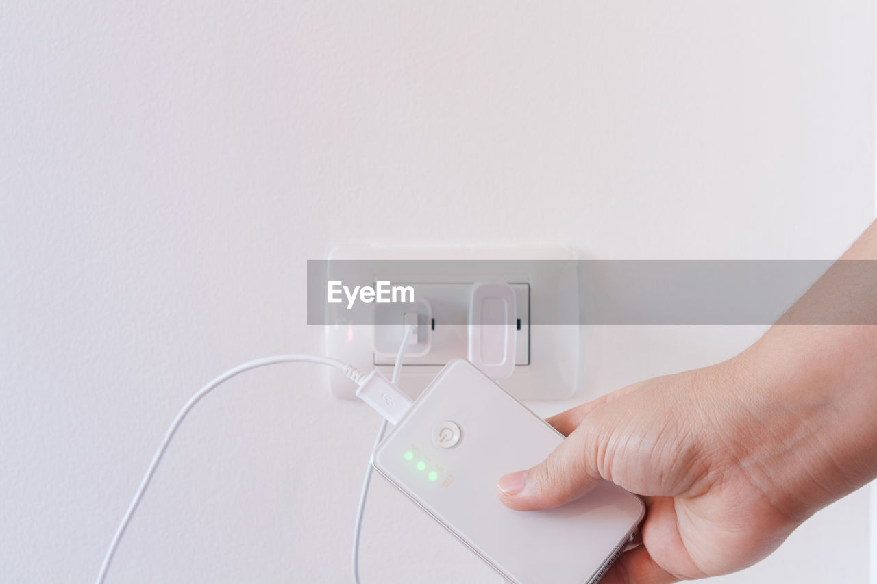 Cropped hand holding portable charger against white background