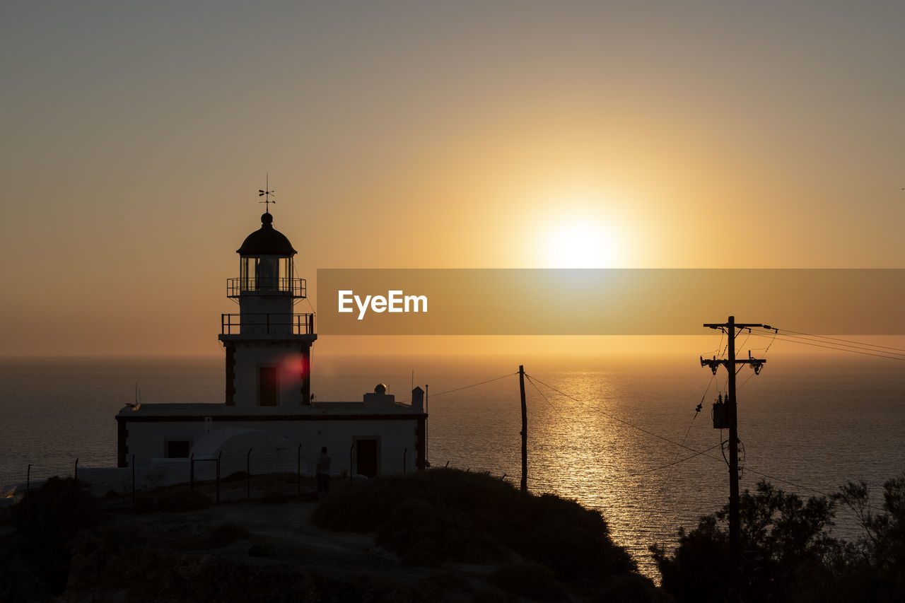 Lighthouse by sea against sky during sunset