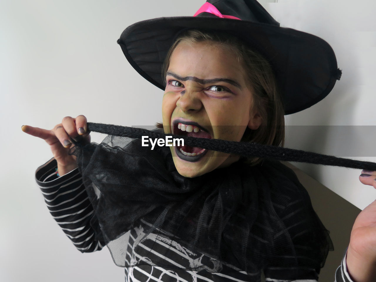 Portrait of girl wearing witch costume and hat biting cloth against wall at halloween