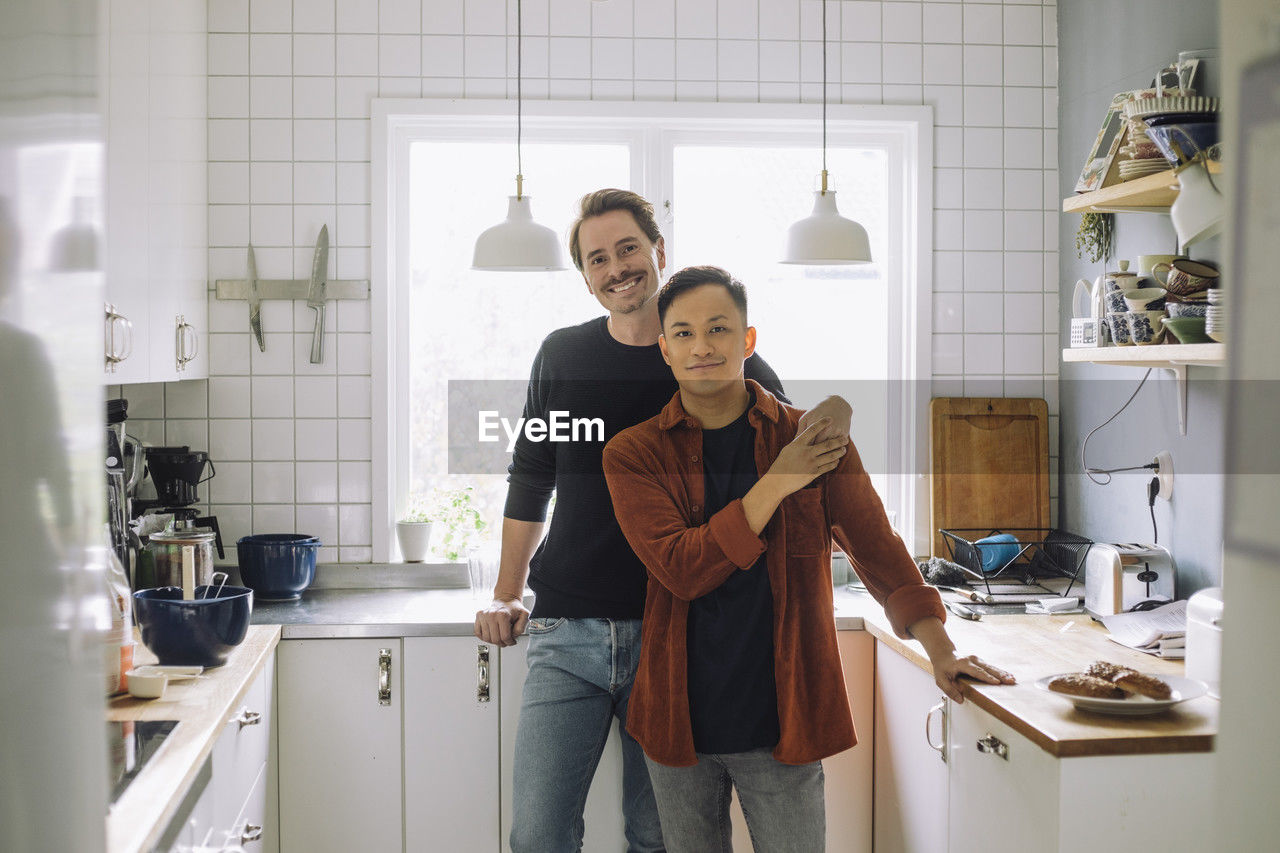 Portrait of smiling multiracial gay couple standing in kitchen at home