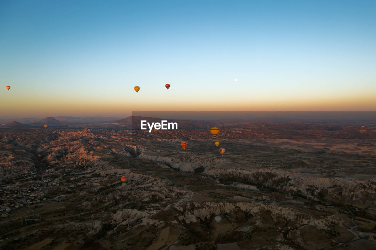 Hot air balloons flying over cappadocia against clear sky during sunset