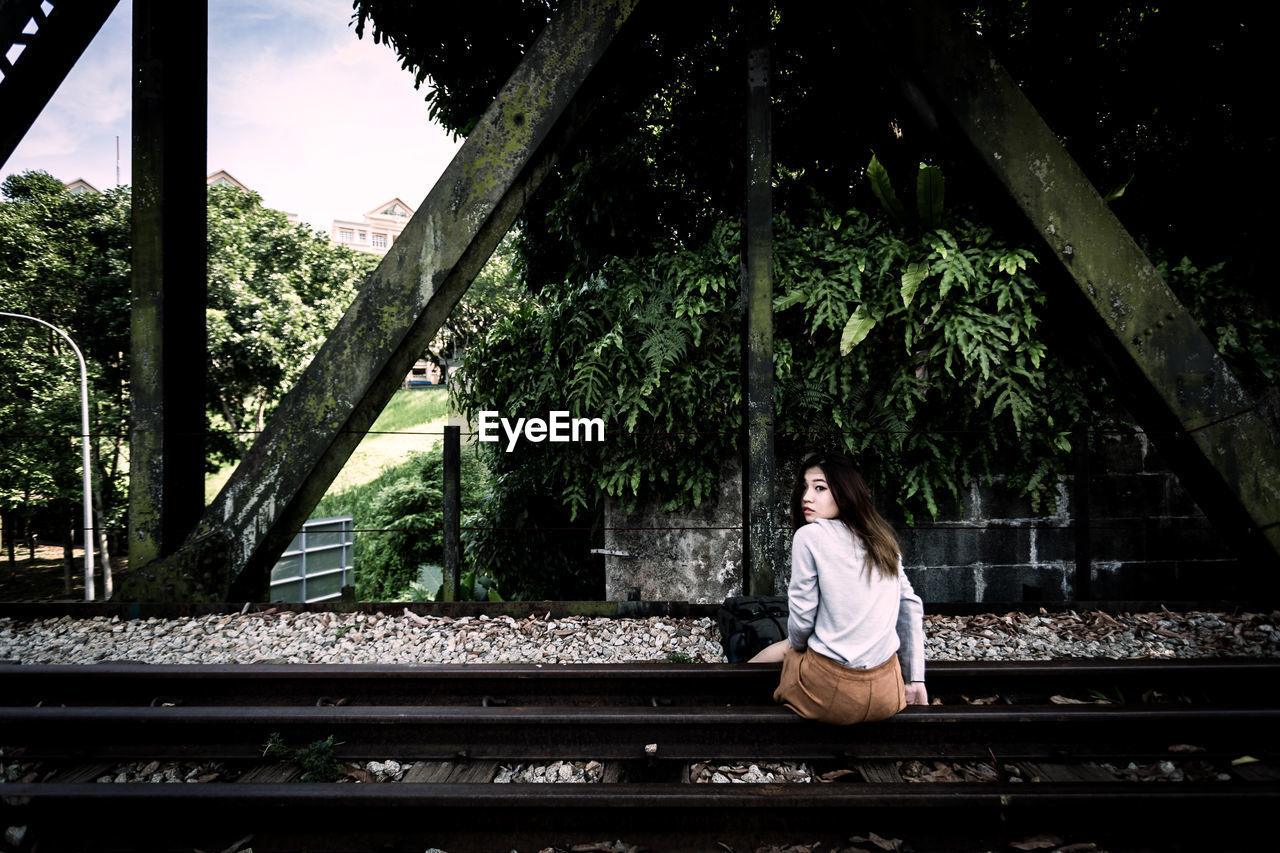 Rear view of woman sitting on railroad track