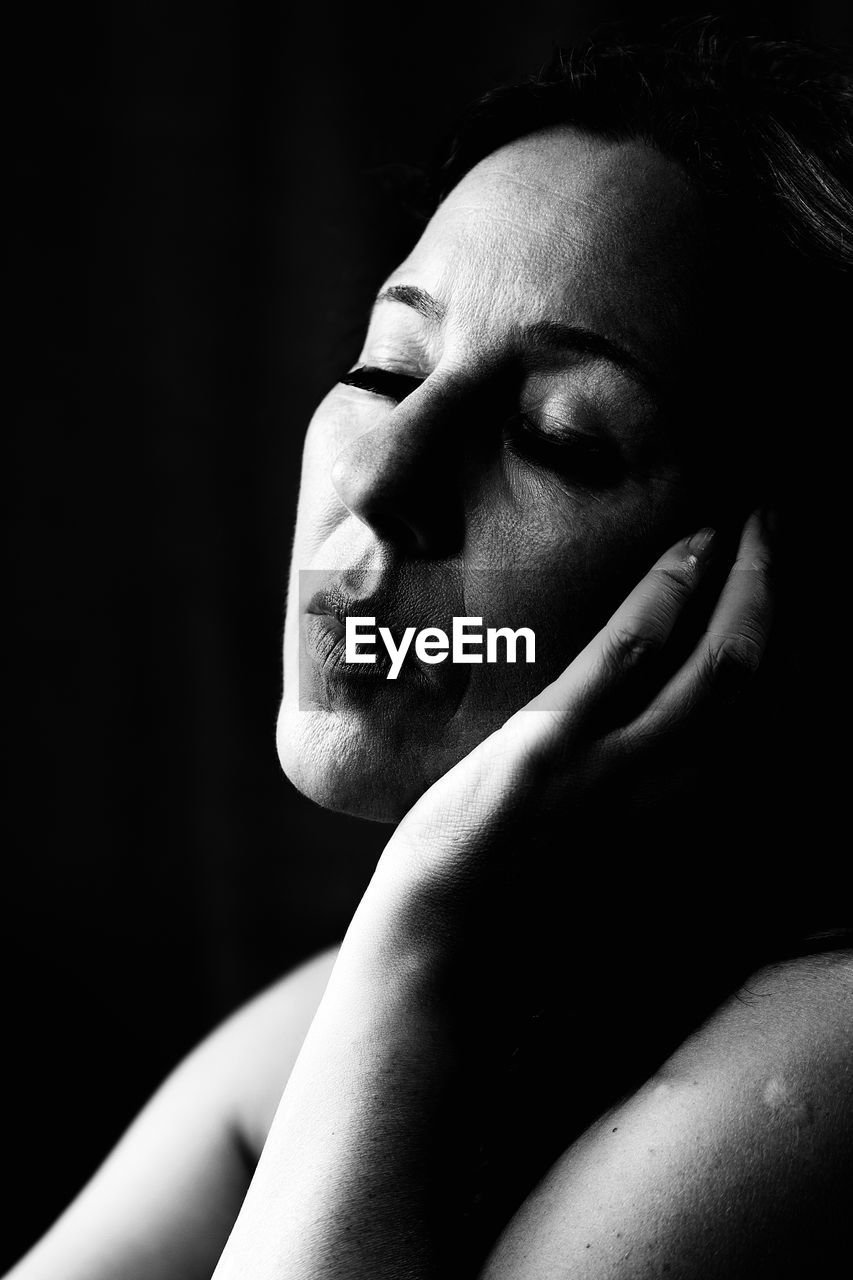 Close-up of woman with closed eyes sitting against black background