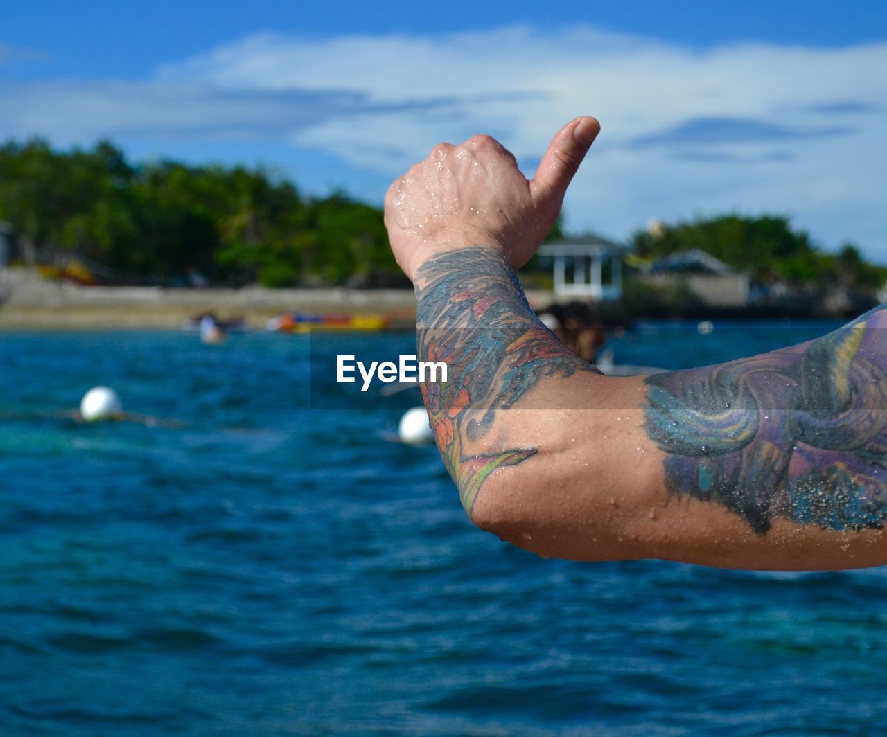 Cropped image of man with tattooed hand gesturing thumbs up sign at beach