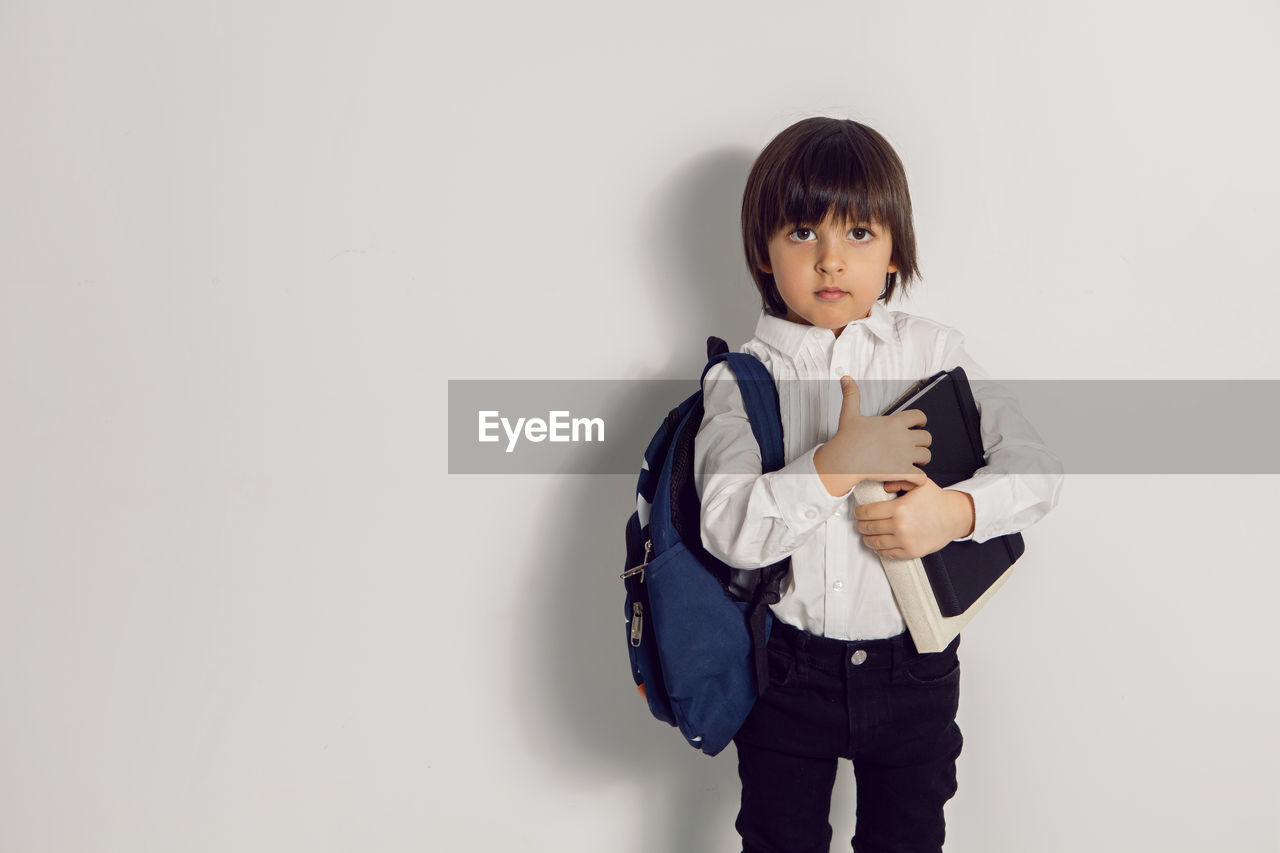 Child boy with a book textbook and backpack stands on a white background