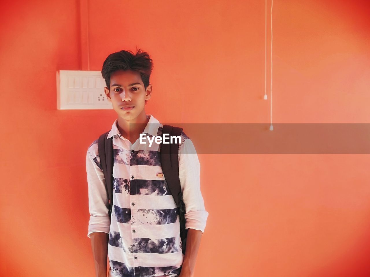 Portrait of young man standing against orange wall