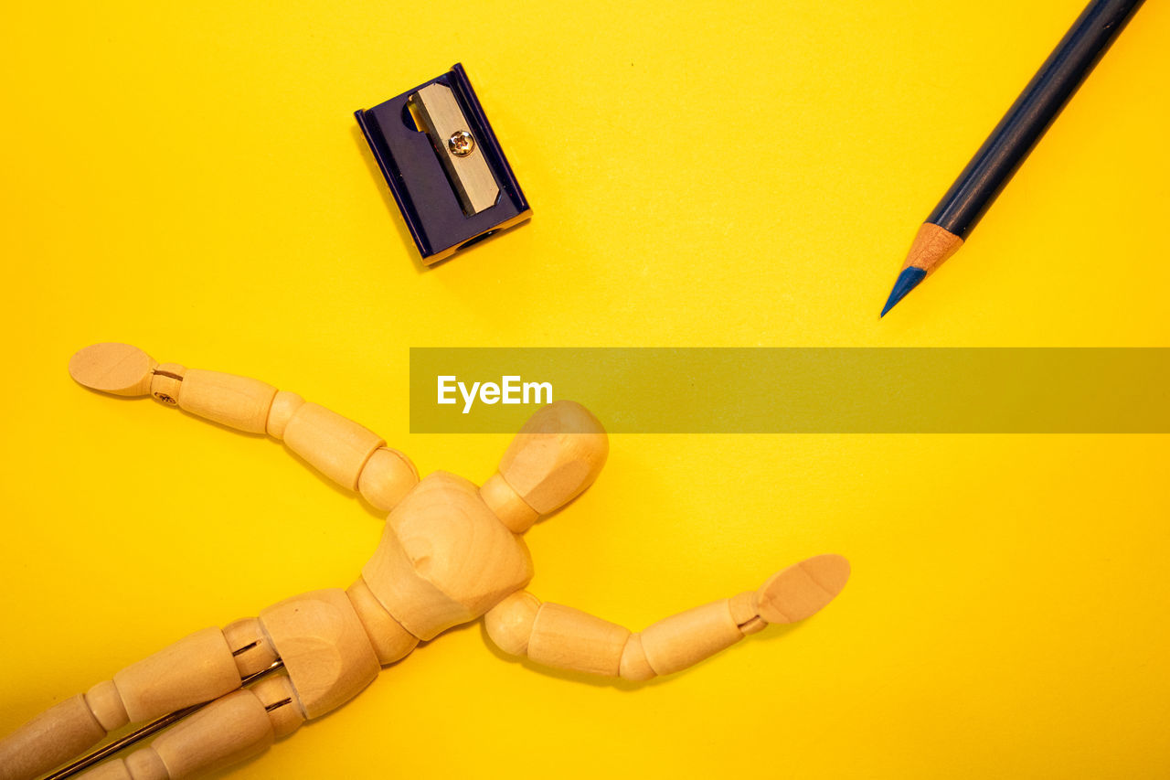 Close-up of figurine with pencil and sharpener on yellow background