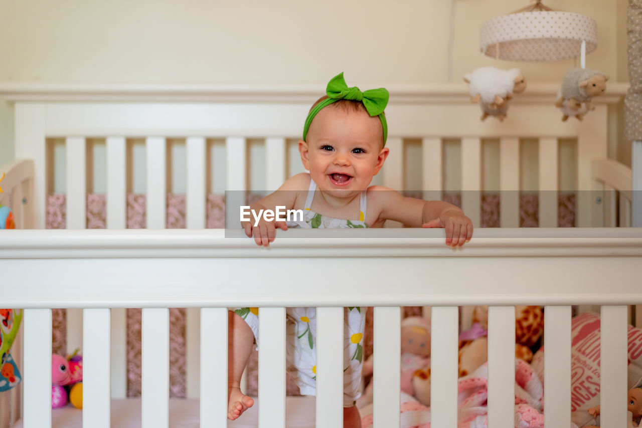 Portrait of happy baby girl standing in crib at home