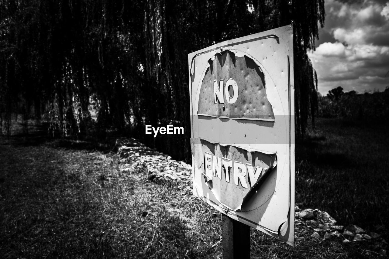 CLOSE-UP OF ABANDONED SIGN ON FIELD BY TREE