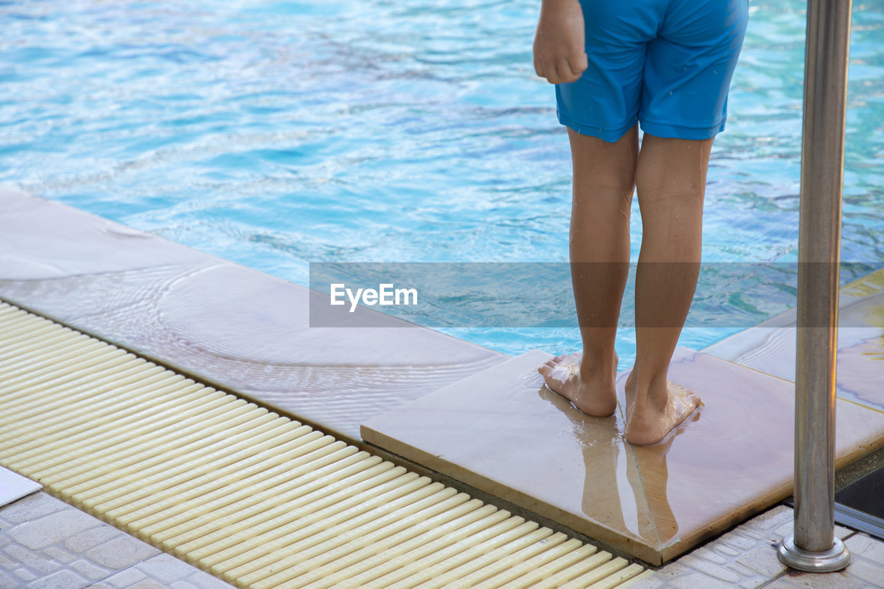 Low section of wet person standing by swimming pool