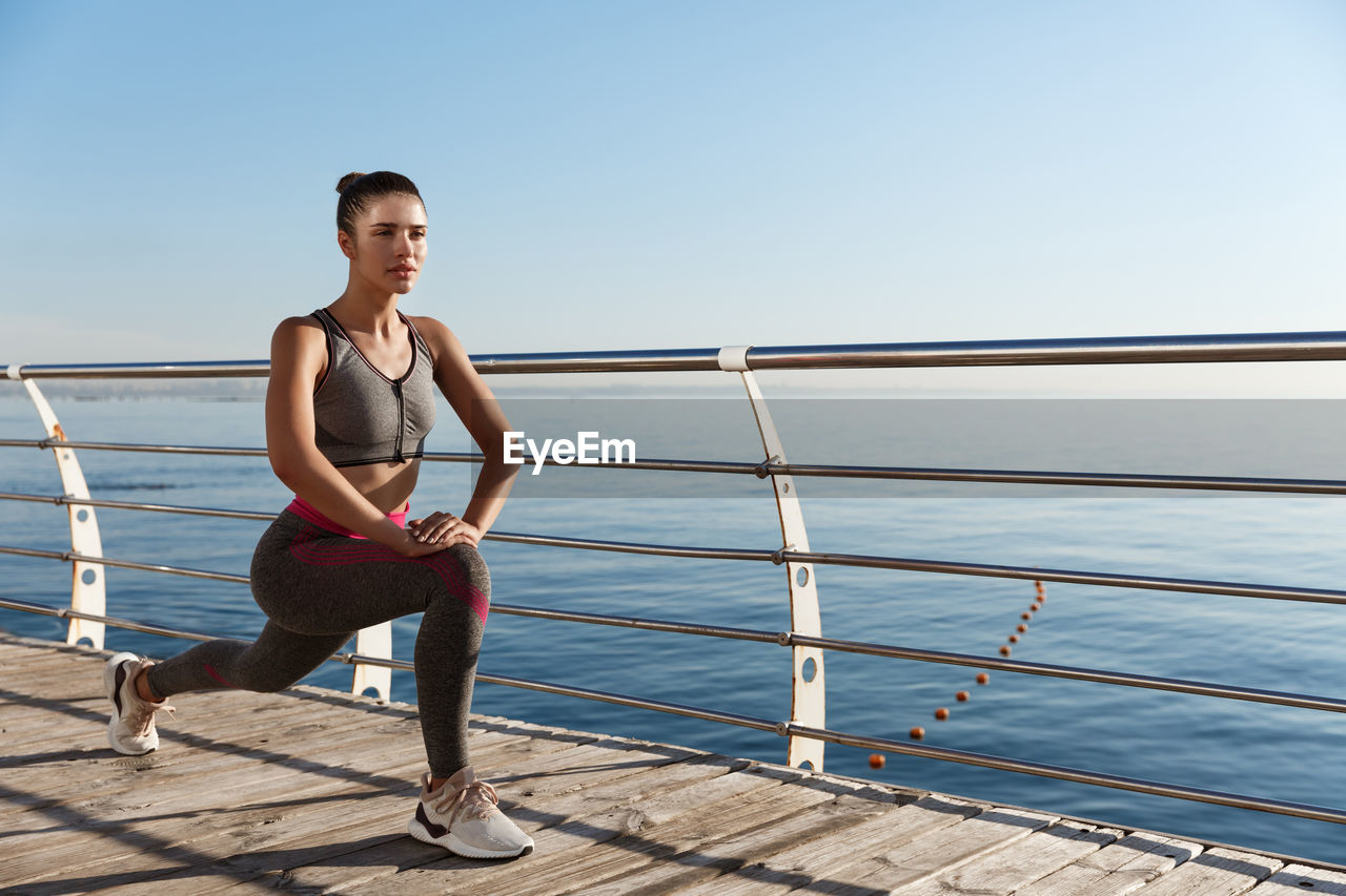 Full length of woman standing by railing against sea